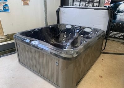 Brown outdoor hot tub with multiple jet seats, open lid, shown in a showroom.