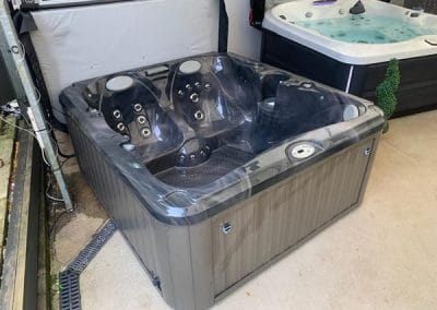 Gray outdoor hot tub with multiple seats and built-in jets on a concrete floor, in a showroom setting.