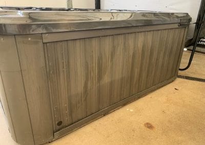 Gray rectangular hot tub with a closed lid, standing on a concrete floor in a garage-like space.